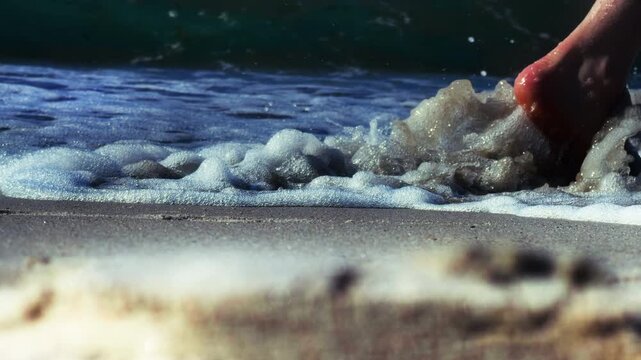 Bare feet walking sandy beach sea waves. Low angle close-up shot capturing people walking along coastline with foaming water washing over shore lifestyle and vacation footage for tourism and travel