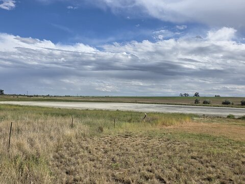 View of Little Gaynor Lake surrounded by grassy fields under a dramatic cloudy sky in Longmont, Colorado, United States.