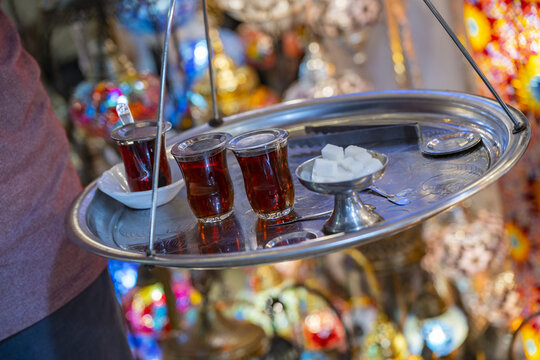 View of a person carrying a traditional metal tray with glasses of Turkish tea and sugar cubes in a vibrant bazaar in Istanbul, Istanbul, Turkiye.