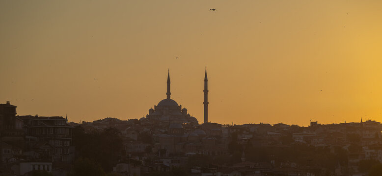 View of the silhouette of a mosque with minarets against a golden sunset sky over the city skyline in Istanbul, Istanbul, Turkiye.