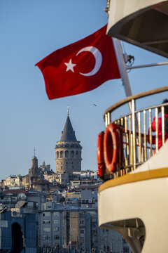 View of Galata Tower rising above the historic urban skyline of Istanbul with a Turkish flag waving in the foreground from a boat deck in Istanbul, Istanbul, Turkiye.