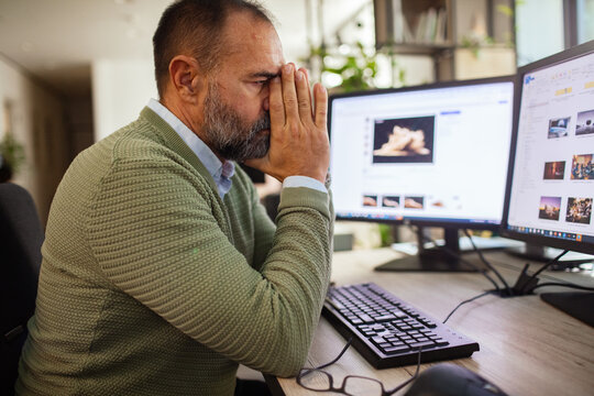 Stressed middle-aged man working at dual monitors in office