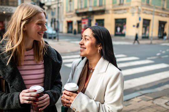 Two women chatting with coffee at a city crosswalk