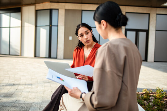 Two businesswomen discussing reports outside office