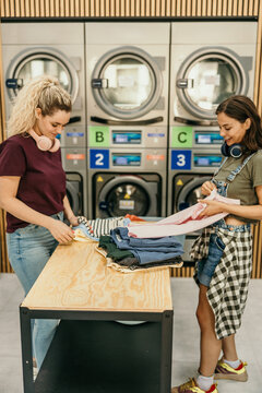 Friends folding clean clothes at self-service laundromat