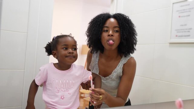 Happy african american mother teaching her cute toddler daughter how to brush her teeth in the bathroom. Family morning routine and oral care