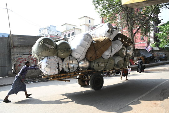 Dhaka, Dhaka Division, Bangladesh - 14 September 2026: View of a man pushing a cart heavily loaded with large bundled sacks along a street.