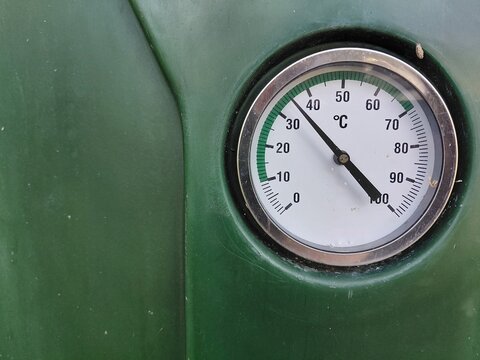 Close-up photograph of an analog temperature gauge with a Celsius scale mounted on a dark green panel