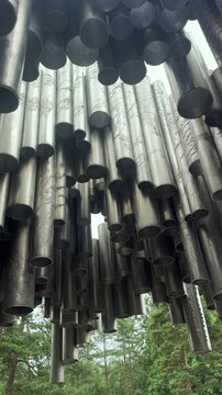 Upward panning detail shot of the abstract stainless steel pipe structure of the famous Sibelius Monument surrounded by pine trees in Helsinki, Finland.