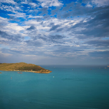 Panoramic aerial seascape with a bulk cargo ship sailing near Quy Nhon, Vietnam. Blue sea, blue sky with white clouds, distant cape with lighthouse and peaceful coastal scenery.