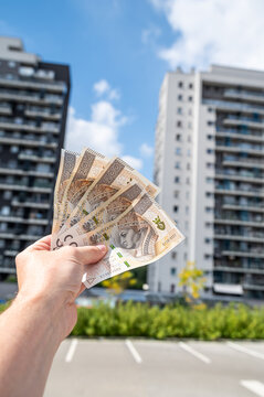 Male Hand Holding Polish Zloty Money Bills in Front of Modern Residential Skyscraper Vertical