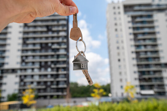 Open Palm Holding House Keys with Metal Keychain and Modern Building Construction Background