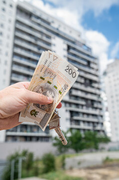 Male Hand Holding Keys and Polish Zloty Bills in Front of High Rise Apartment Building Vertical