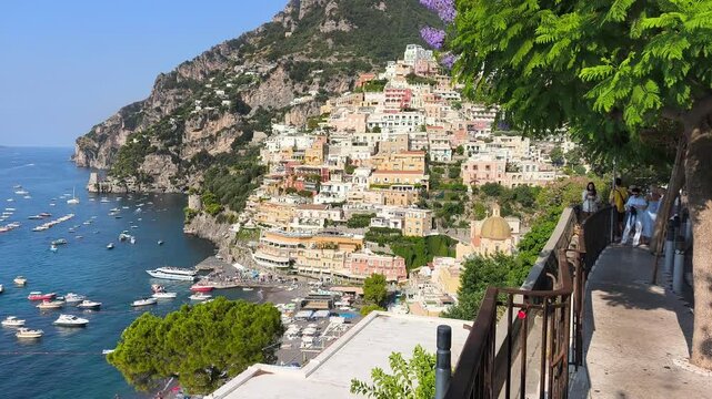Scenic view of Positano village on Amalfi Coast framed by blooming purple Jacaranda flowers and green leaves in foreground, Italy