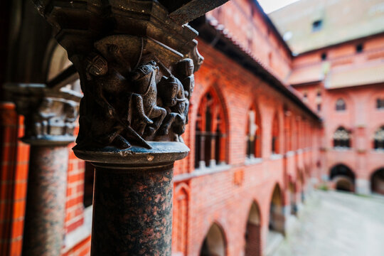Malbork, Pomeranian Voivodeship, Poland - 23 March 2026: View of an intricately carved stone pillar with knights on horseback in the historic red brick courtyard of Malbork.