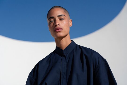 Minimal portrait of a confident woman with shaved head and circular sky backdrop for beauty banner and editorial layout