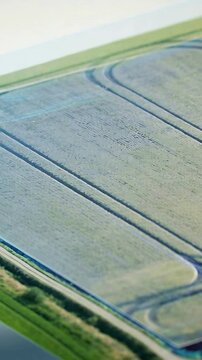 Vertical video: Panning drone surveying crop field diagonal with twin tracks, arc, hedge, ditch