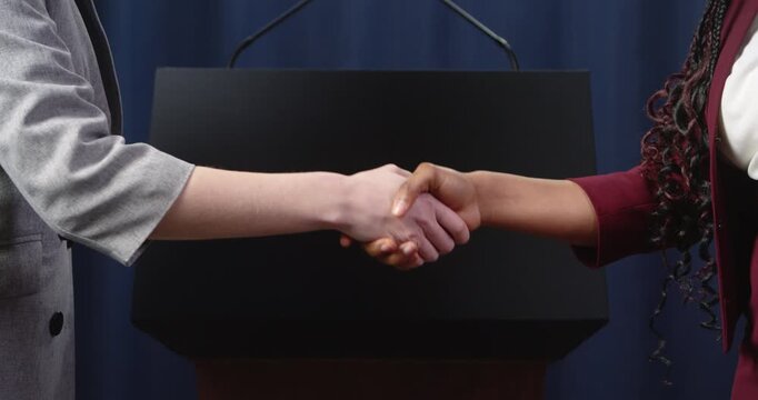 Podium with microphones is followed by a handshake between two people, symbolizing political negotiations, public agreement, diplomacy and cooperation