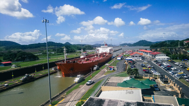 Panama - 13 September 2026: View of a large cargo ship navigating through the Panama Canal locks, surrounded by lush green hills under a bright blue sky with scattered clouds.