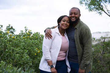 Obraz premium African couple standing among coastal shrubs near sandy dunes, wearing jeans jacket and smartwatch