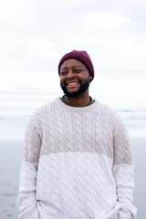Obraz premium African man standing on wet sand shore, wearing maroon beanie and cream cable knit sweater