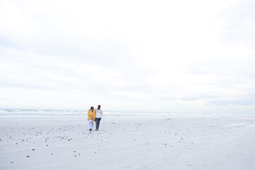 Obraz premium African American couple walking shore near ocean, stones prints, yellow jacket, burgundy beanie