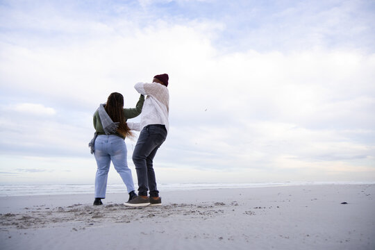 African American couple walking on wide sandy beach at shoreline, wearing jackets and beanie
