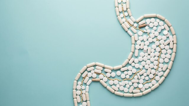 Stomach shape made of medical pills and capsules, digestive health concept with medication, human gastric system anatomy on blue background