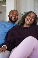 Obraz premium African American couple laughing, leaning on couch at home, woman in maroon top, white smartwatch
