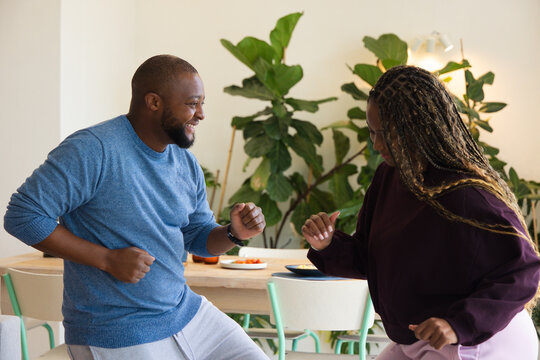 African American couple dancing in dining area by wooden table with sliced fruit and wristwatch