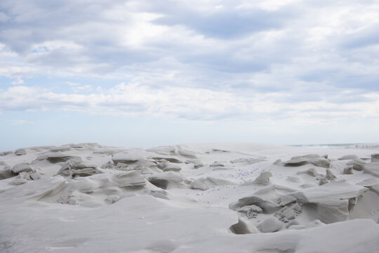 Wind-sculpted rocks are forming pebbled coastal sand flats with shallow hollows under cloudy sky