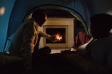 Obraz premium African American adult and youth males sitting in pop-up tent on living room rug facing fireplace