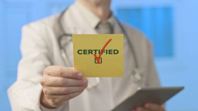 Doctor in a white coat and stethoscope holding a yellow sticky note with certified and a red checkmark, symbolizing professional qualification and healthcare approval