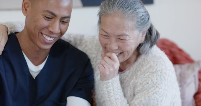 Senior Asian woman and African man smiling touching shoulder on sofa man pointing at tablet showing