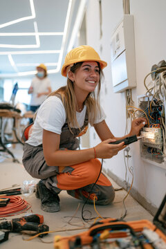 Female electrician in hard hat working on smart home electrical panel with tools