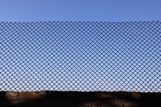 Looking up at a chain link fence with blue sky and clouds. wire fence. Chain link fence see sky. Opening in metallic fence. blue sky. Challenge. breakthrough concept.