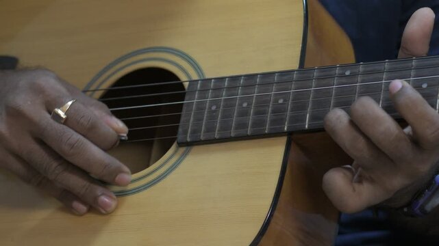guitarist's hands picking strings and holding chord positions on the fretboard of a natural wood acoustic guitar