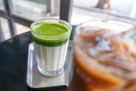 Layered matcha latte with bright green matcha tea over cold milk served in a glass at modern cafe in Thailand. Trendy Asian beverage, cafe culture, healthy lifestyle, specialty drinks