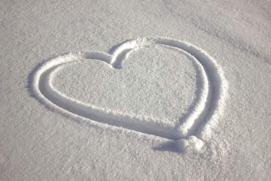 Hand drawn Heart shape in fresh white snow during winter day, romantic love concept background.