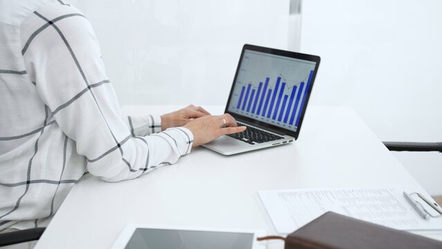 Businesswoman's hands typing on a laptop keyboard displaying financial graphs and bar charts, analyzing market data and performance metrics to inform strategic decisions