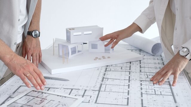 Architects collaborating on building design, analyzing blueprints and a house model, discussing construction plans and urban development ideas in a modern office
