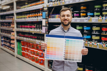 Smiling man holding a paint color palette choosing shades for home renovation in a hardware store...