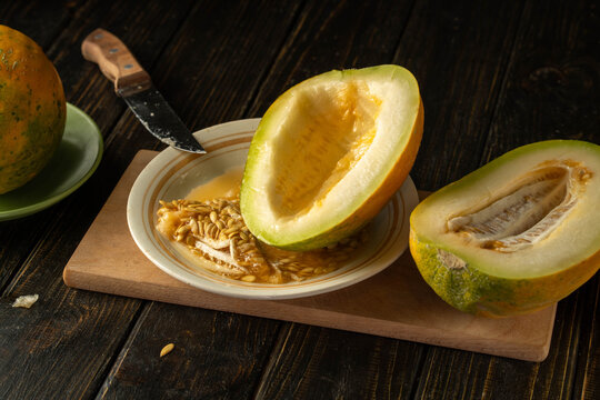 A vibrant melon, freshly cut and revealing its sweet, golden flesh, sits beside a knife on a rustic wooden table. The seeds glisten in the soft light, adding beauty to the scene
