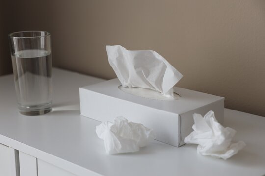 Box with paper tissues, used napkins and glass of water on white cabinet indoors, closeup