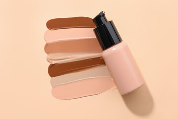 Swatches of different liquid foundations and bottle of makeup product on beige background, top view