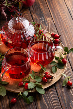 Warm rosehip tea served in glass cups and teapot on a wooden tray with fresh berries