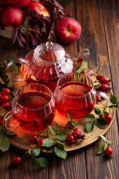 Two glasses and teapot filled with rich red rosehip tea alongside fresh apples and berries