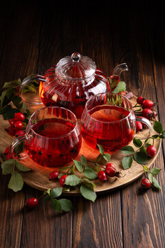Warm Rosehip Tea In Glass Teapot and Cups Surrounded by Fresh Berries and Leaves