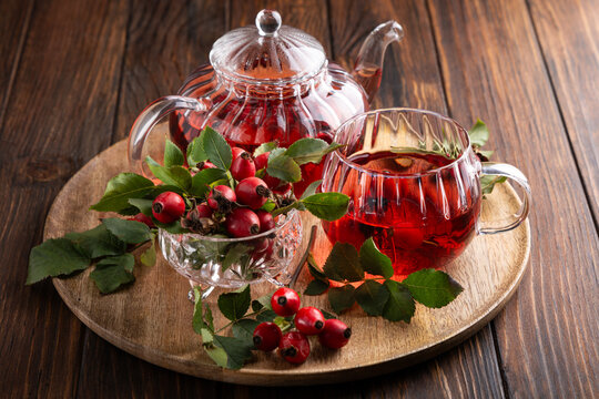 Rosehip tea in glass teapot and cup with fresh berries on wooden table background