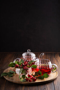 Rosehip tea and berries presented in elegant glass ware on wooden tray with dark background
